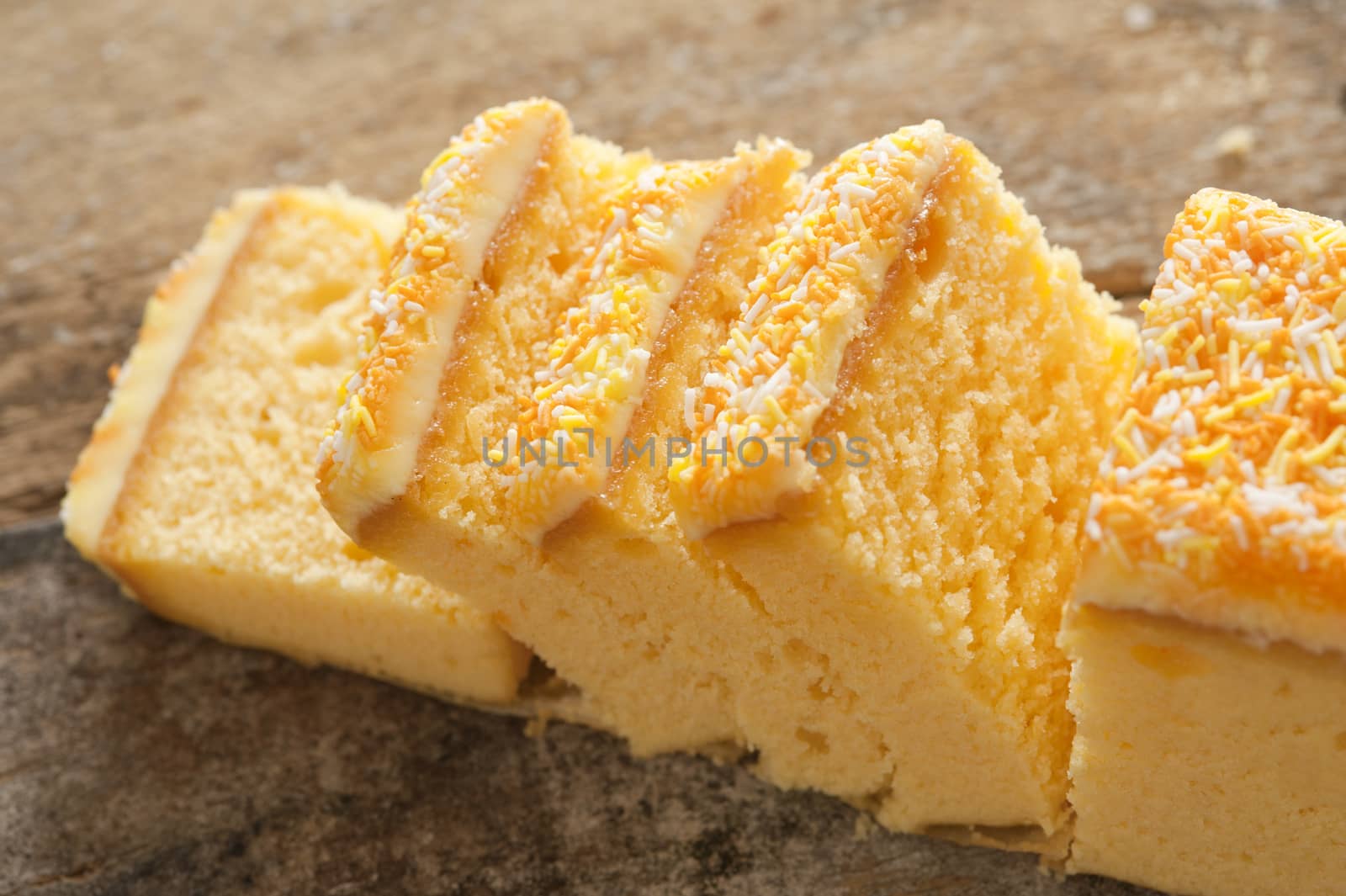 Close up of yellow cake with sprinkles and icing sliced into small portions on a rustic wood table