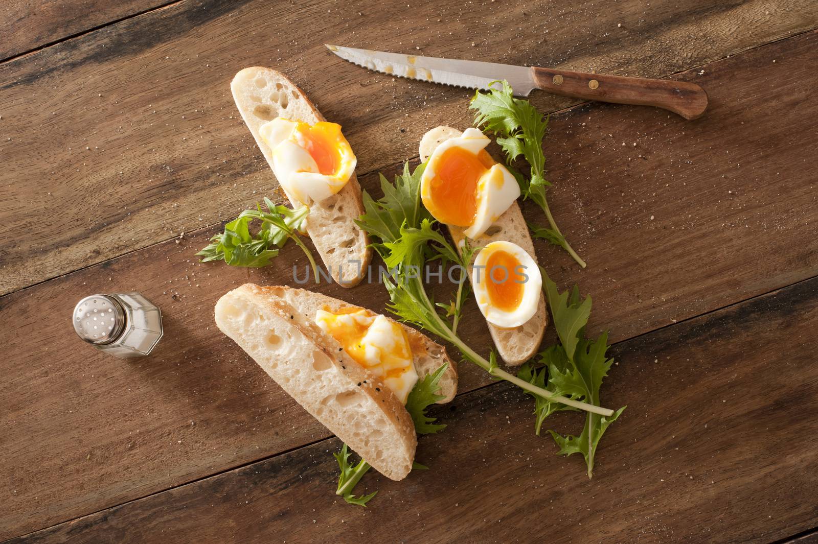 Soft cooked eggs sliced and served on bread beside long stemmed herbs and a serrated knife