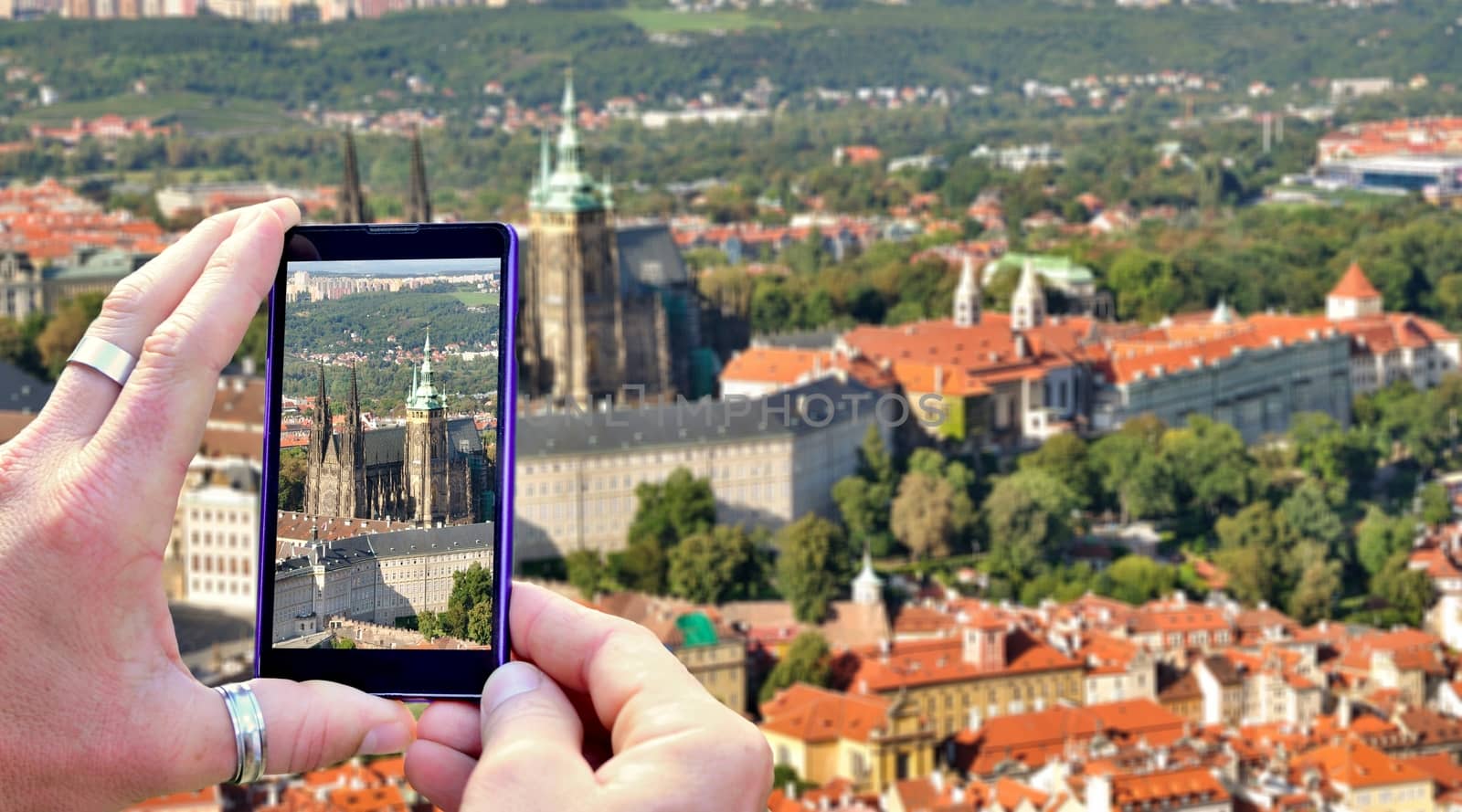 View over the mobile phone display during shooting Prague Castle in Prague. Holding the mobile phone in hands and taking a photo, focused on mobile phone screen.