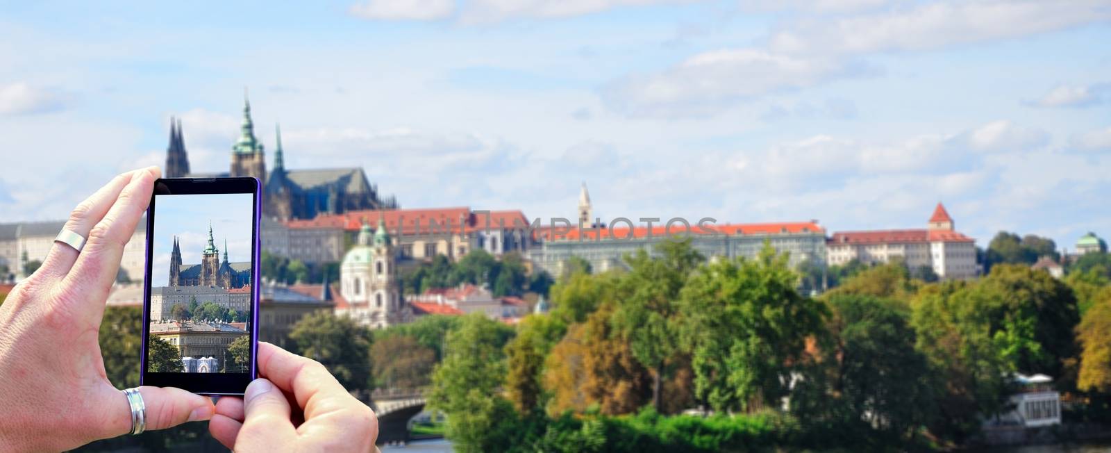 View over the mobile phone display during shooting Prague Castle in Prague. Holding the mobile phone in hands and taking a photo, focused on mobile phone screen.