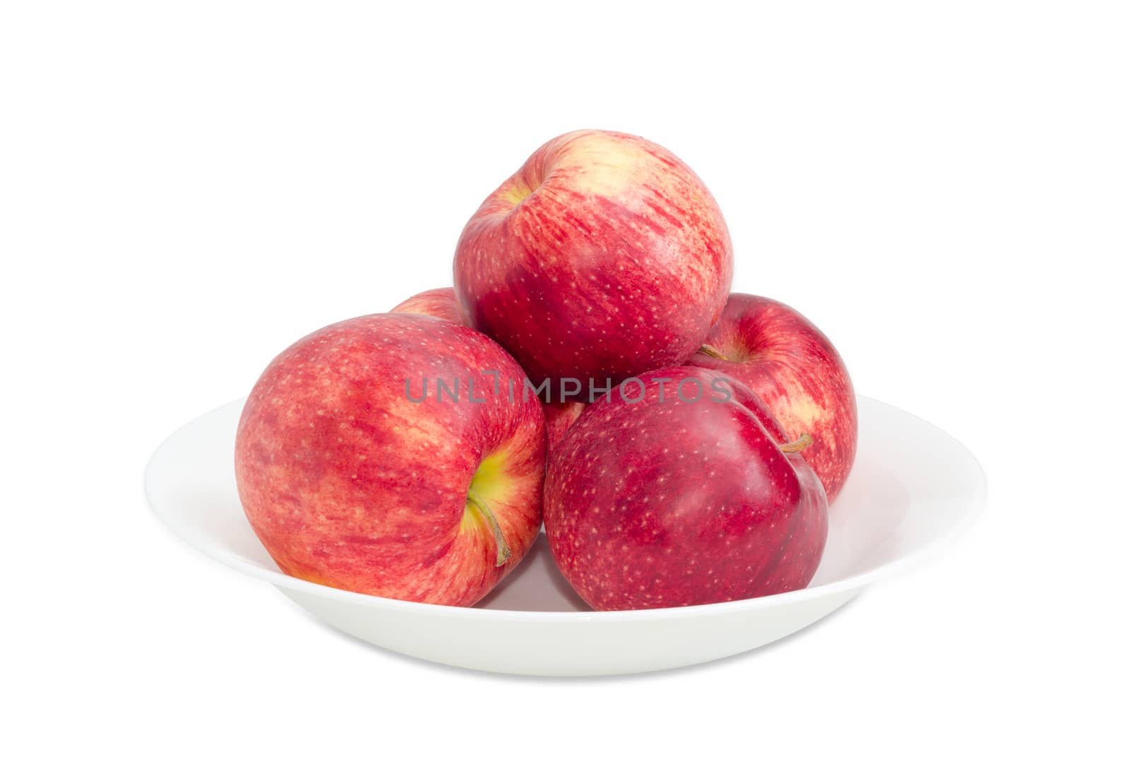 Several red ripe apples on a white dish on a light background closeup 
