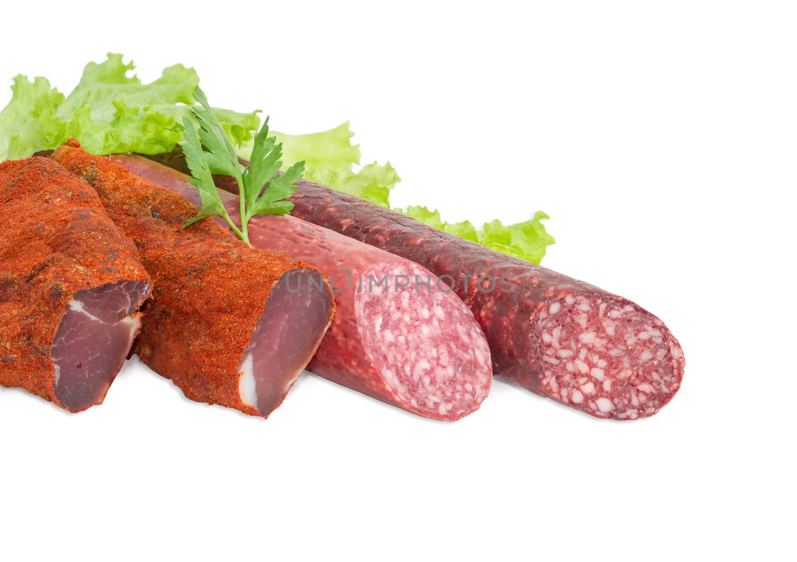 Fragment of the partly sliced two pieces of the dried pork tenderloin and two different dry smoked sausage with parsley twig on the lettuce closeup on a light background  
