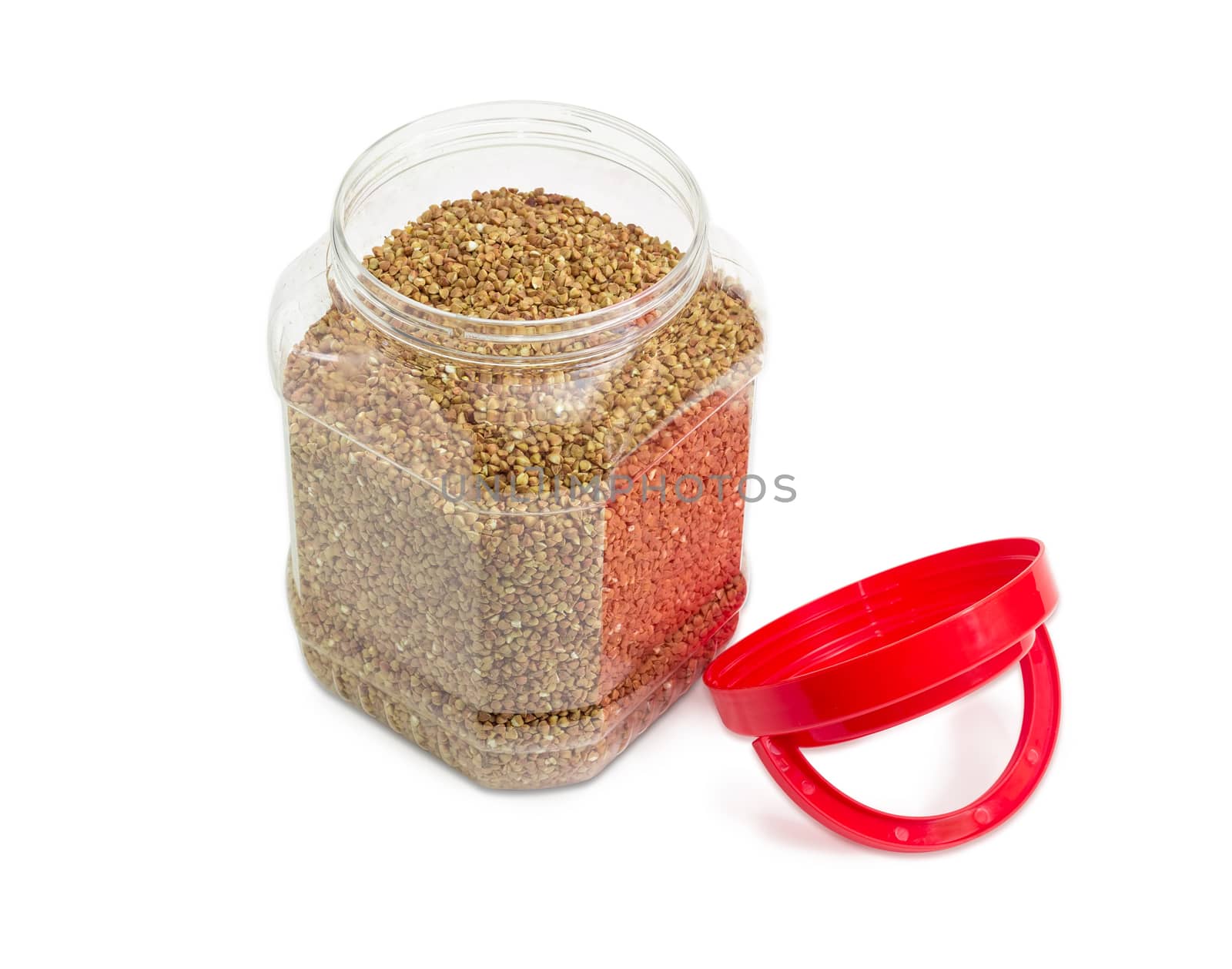 Buckwheat groats peeled from the husk in the transparent plastic container with a red open cover on a light background
