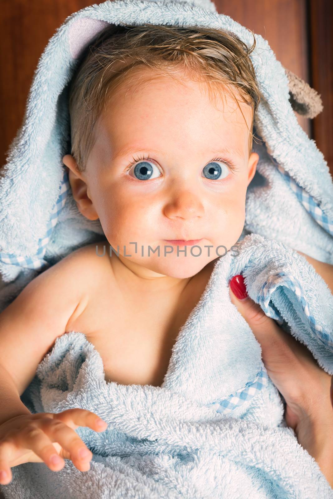 Little pretty wet baby boy bundled up in towel after bath being held by mother,vertical photo.