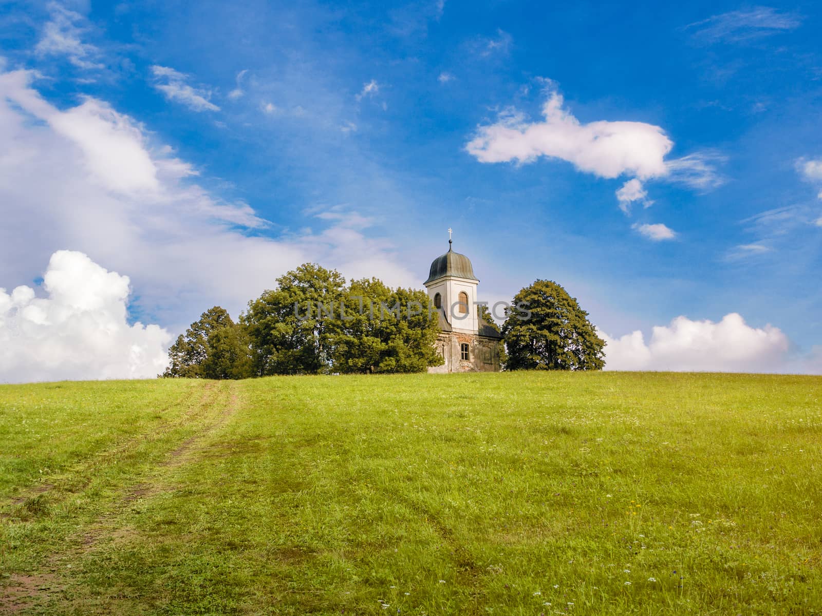 Christian church or chapel with white tower on top of the hill in the forest, horizon between green ground and blue cloudy sky, copy space, relaxing travelling in bright summer day
