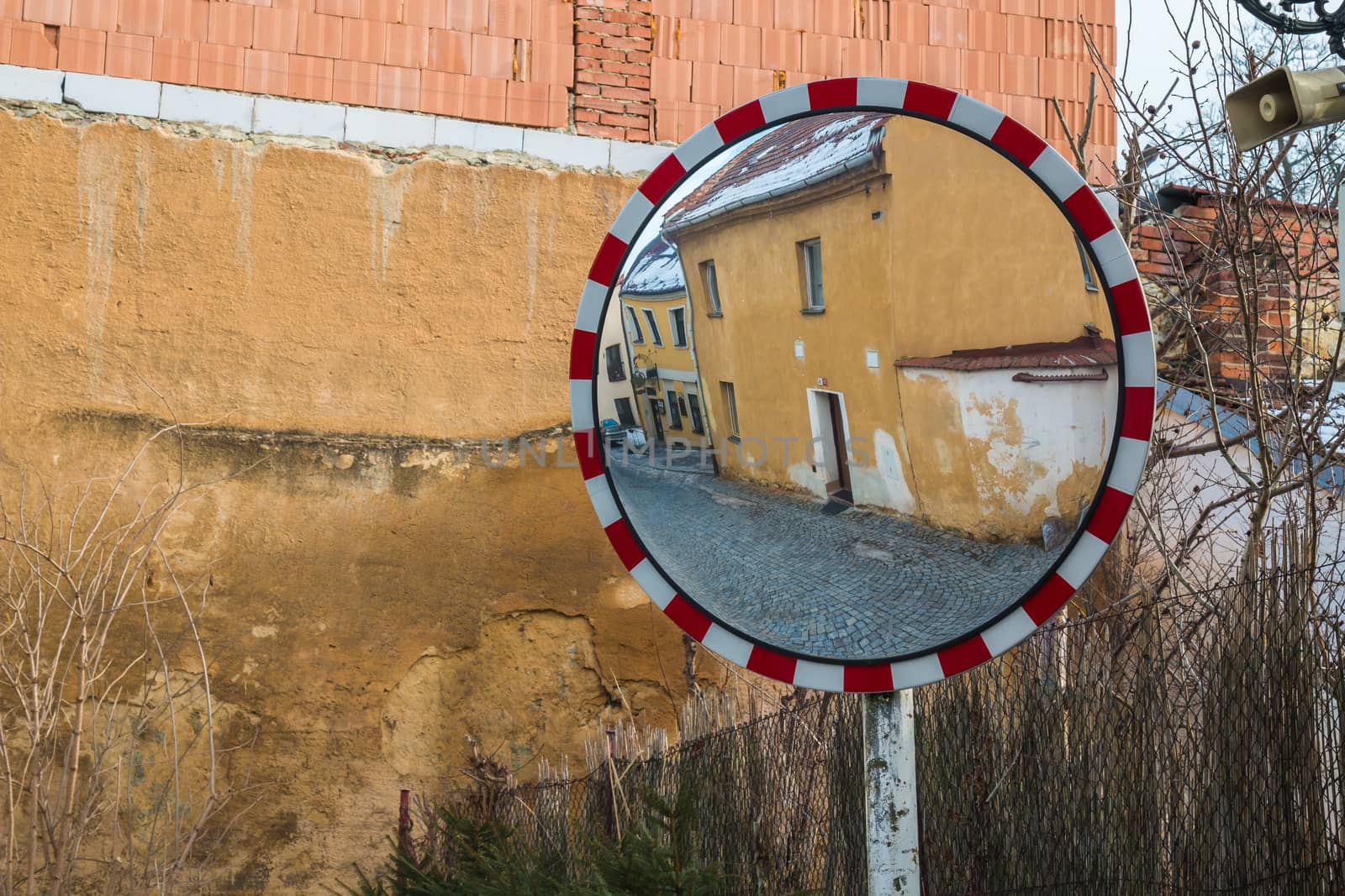 Reflection of the street with old houses in the traffic mirror with red and white frame. Old wall in the background. Boskovice, Moravia, Czech republic.