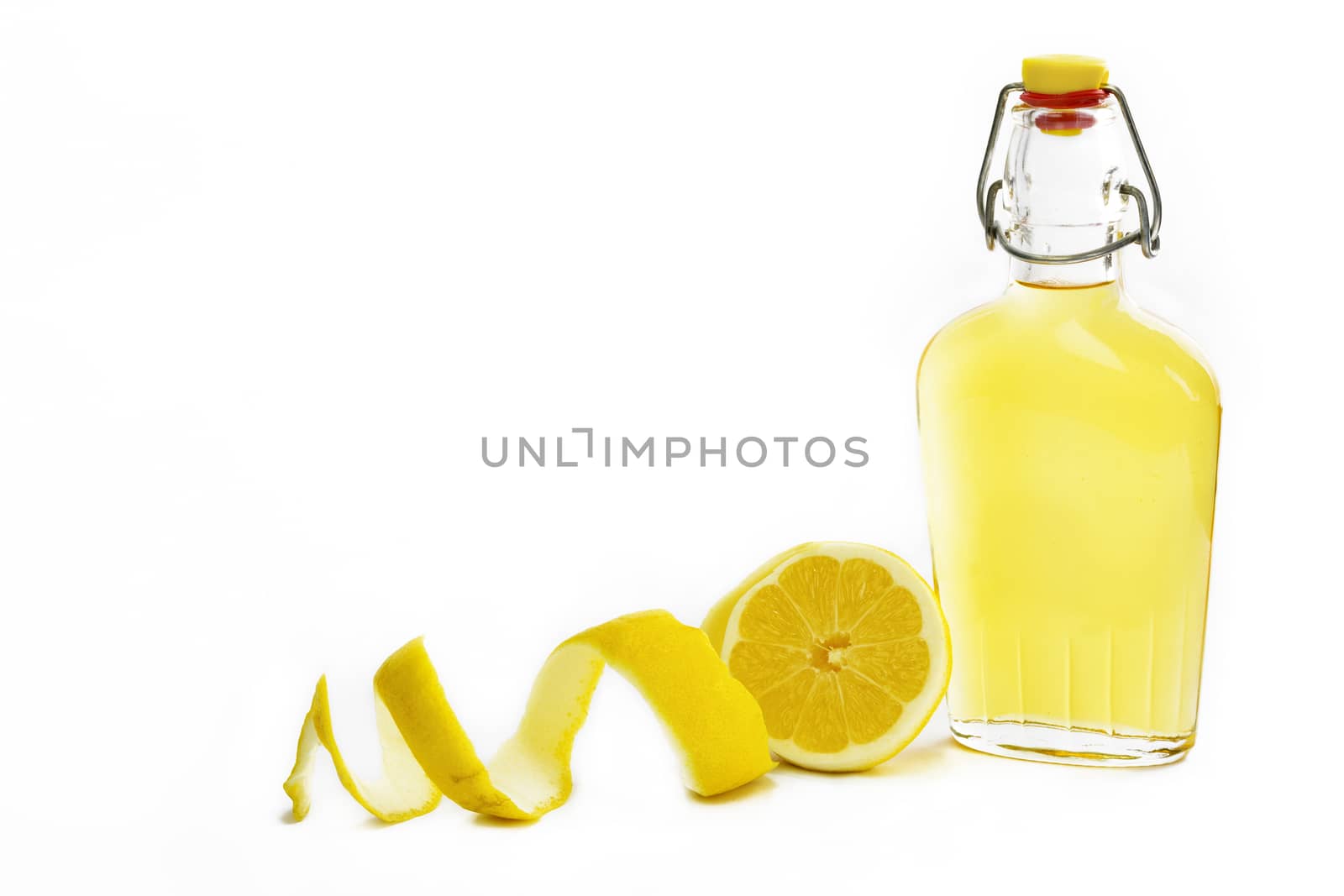 Open glass decanter bottle and shot glass filled with yellow lemon liquor or limoncello or limoncino on white. Peeled natural organic lemon.