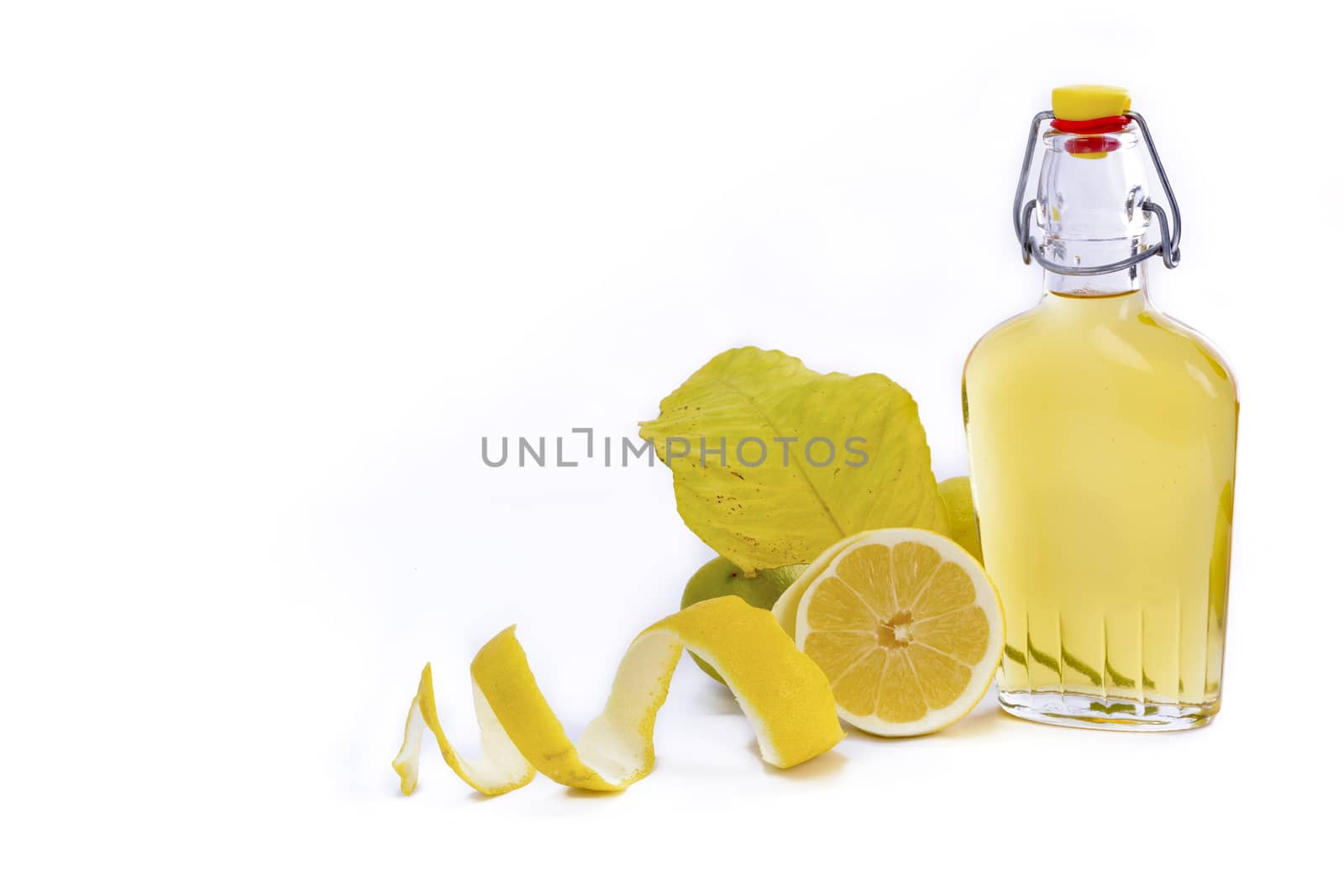 Open glass decanter bottle and shot glass filled with yellow lemon liquor or limoncello or limoncino on white. Peeled natural organic lemon.