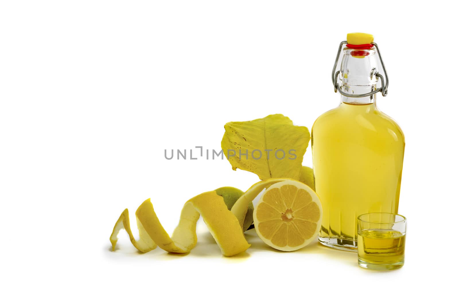 Open glass decanter bottle and shot glass filled with yellow lemon liquor or limoncello or limoncino on white. Peeled natural organic lemon.