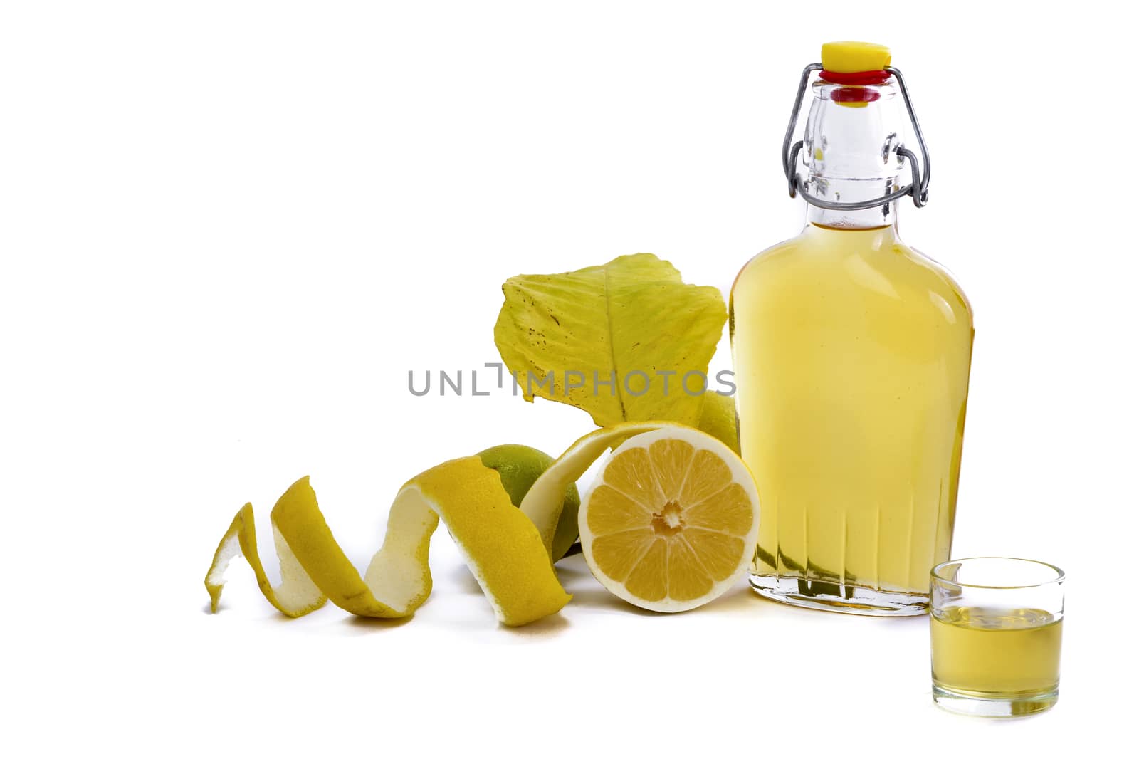 Open glass decanter bottle and shot glass filled with yellow lemon liquor or limoncello or limoncino on white. Peeled natural organic lemon.