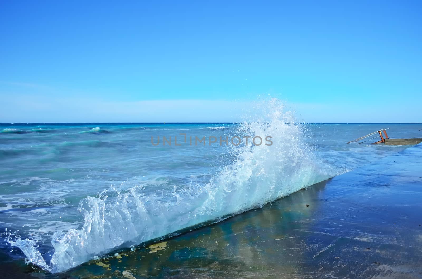 Powerful waves of the sea foam, breaking the concrete pier