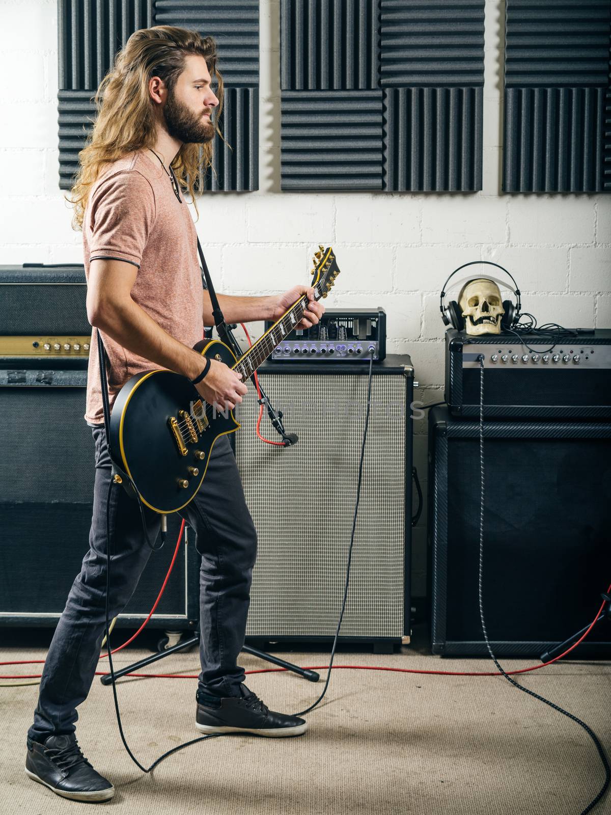 Photo of an attractive man playing electric guitar in a recording studio.