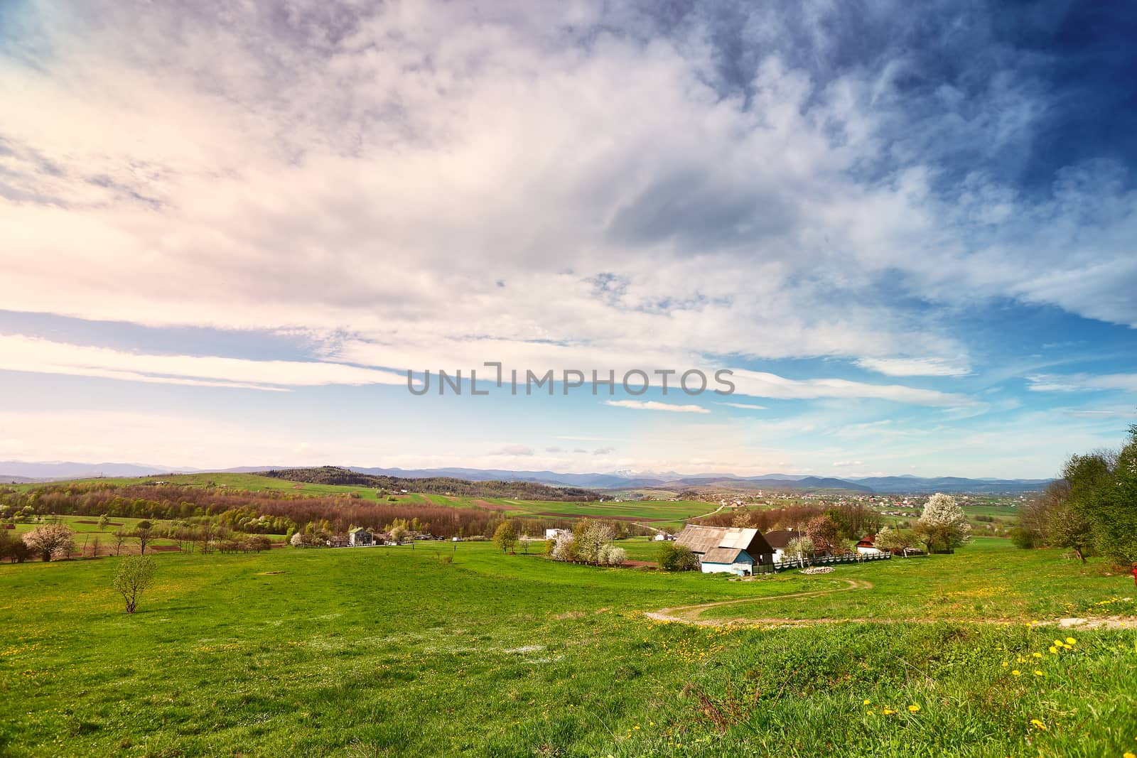 Sunny spring day in village and town on foothills. Mountains on background. Sunny green spring landscape.