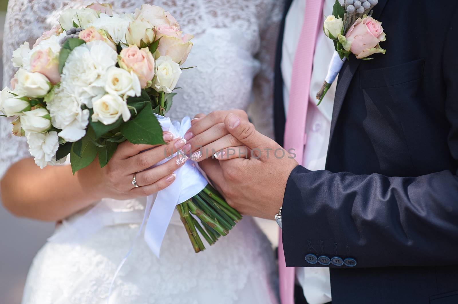 groom holds his brides hand and a wedding bouquet close up