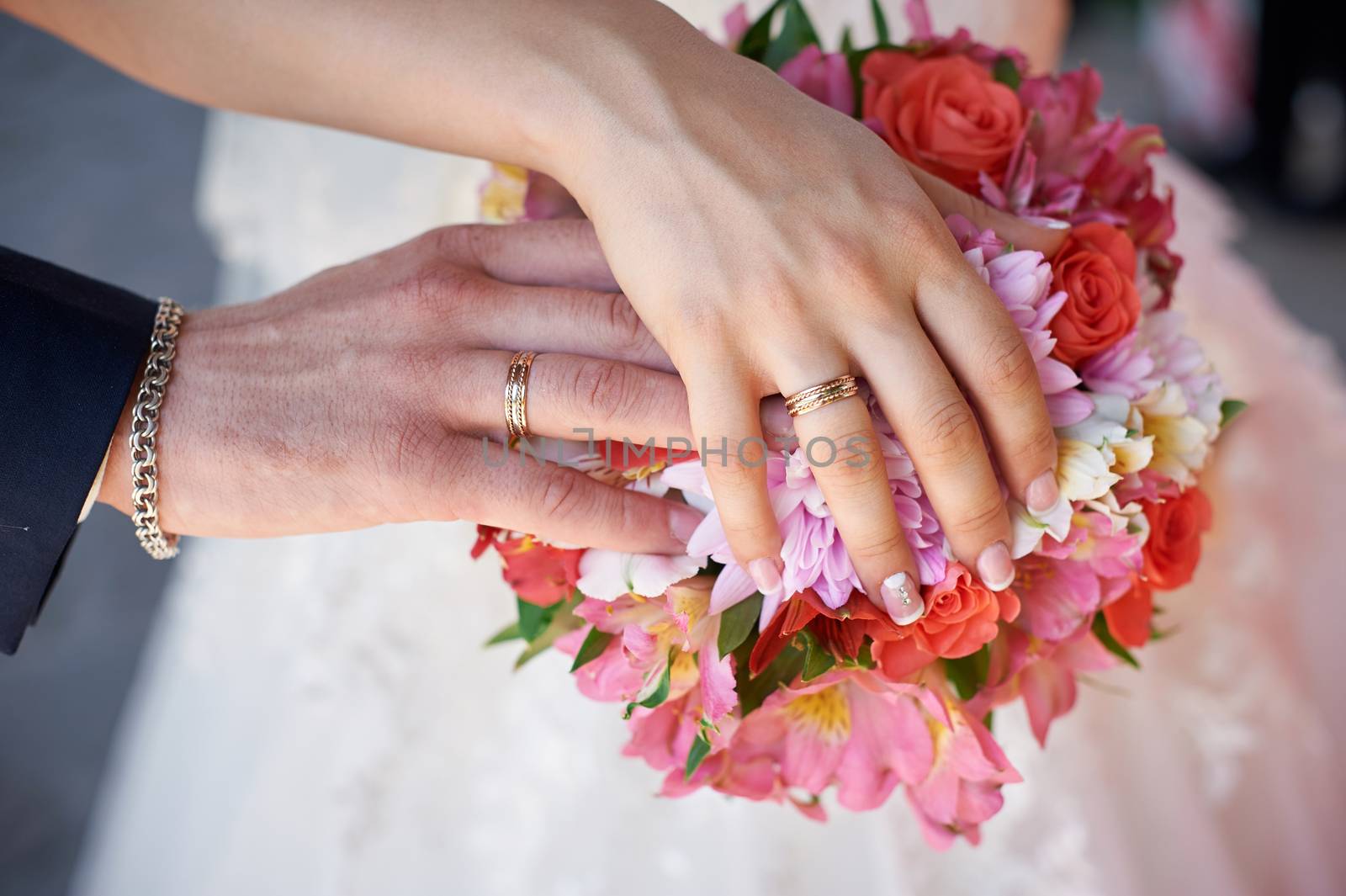 bride and groom hand with rings on wedding bouquet.