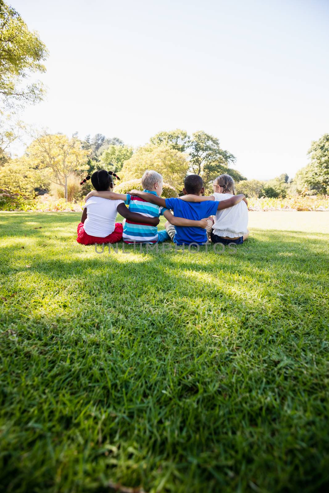 Kids are sitting on the grass together during a sunny day by Wavebreakmedia