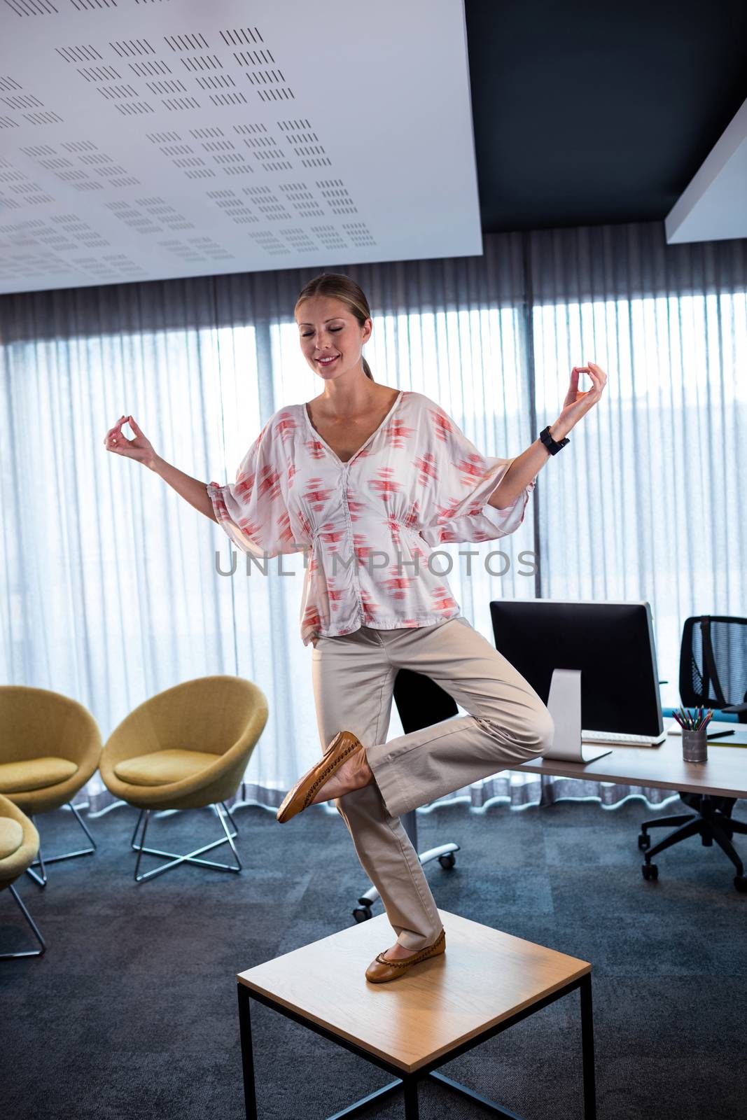 Businesswoman doing yoga on a table by Wavebreakmedia
