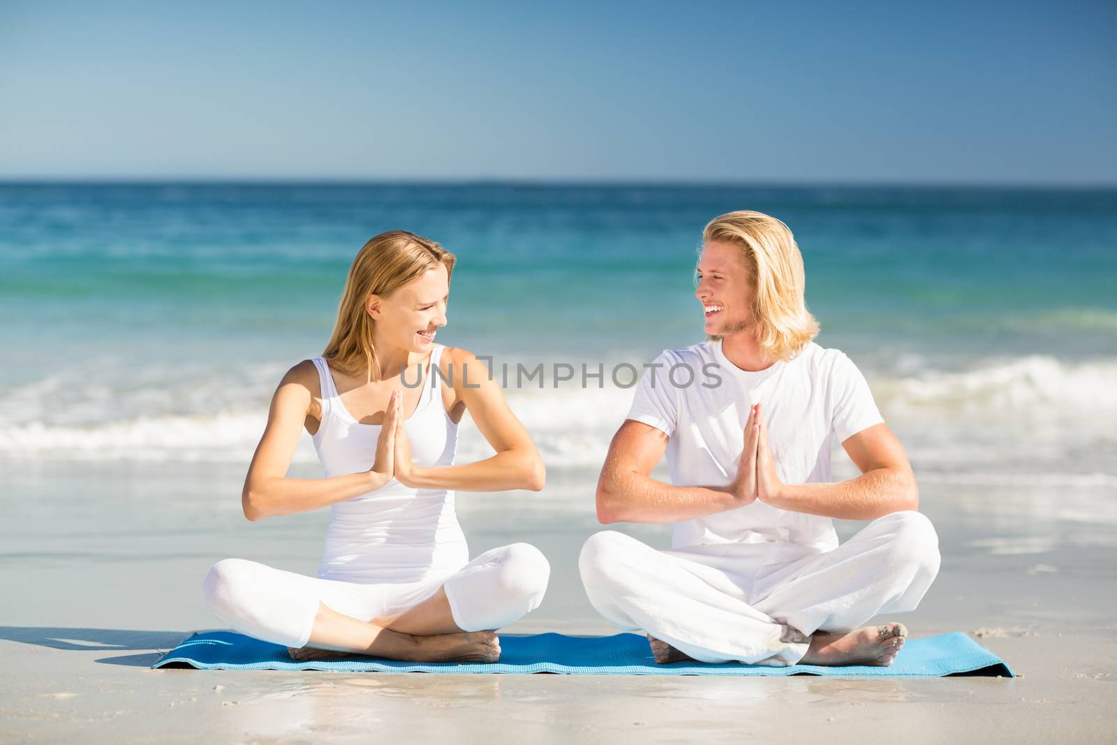 Happy man and woman performing yoga on beach