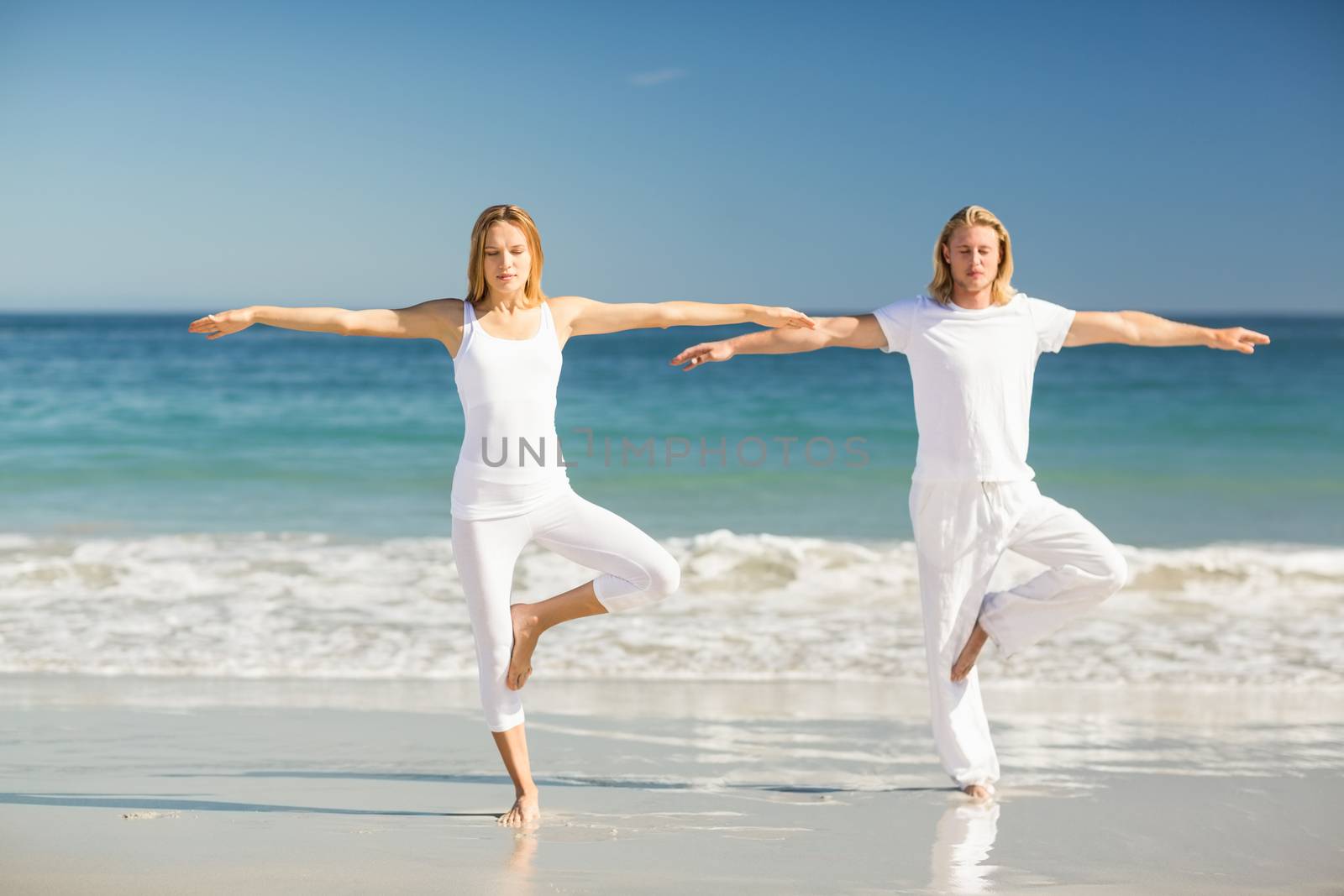 Man and woman performing yoga on beach