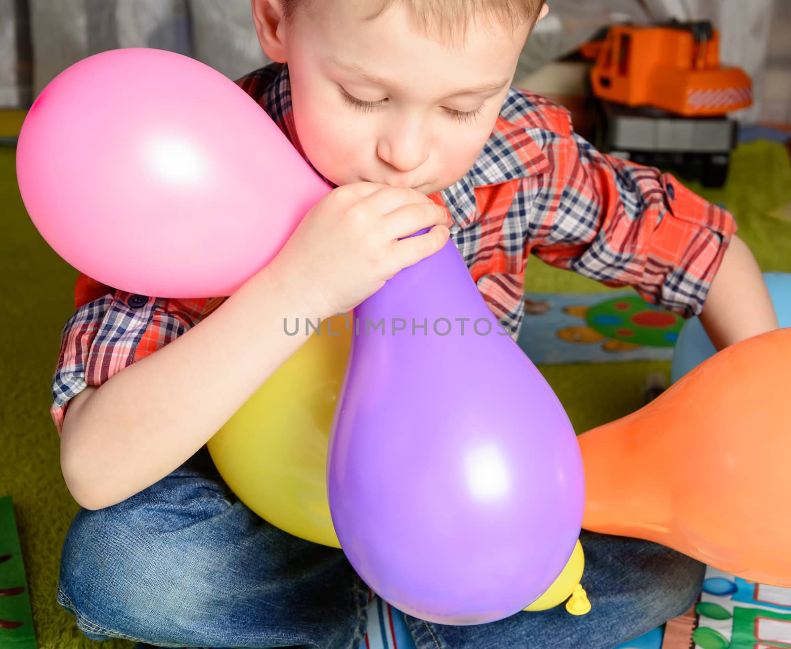 little boy inflates colored balloons sitting on the floor