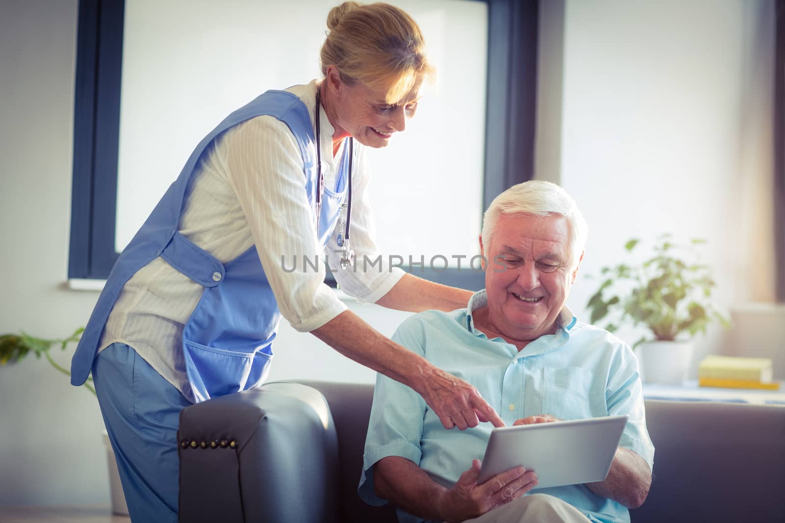 Senior man and female doctor using digital tablet in living room