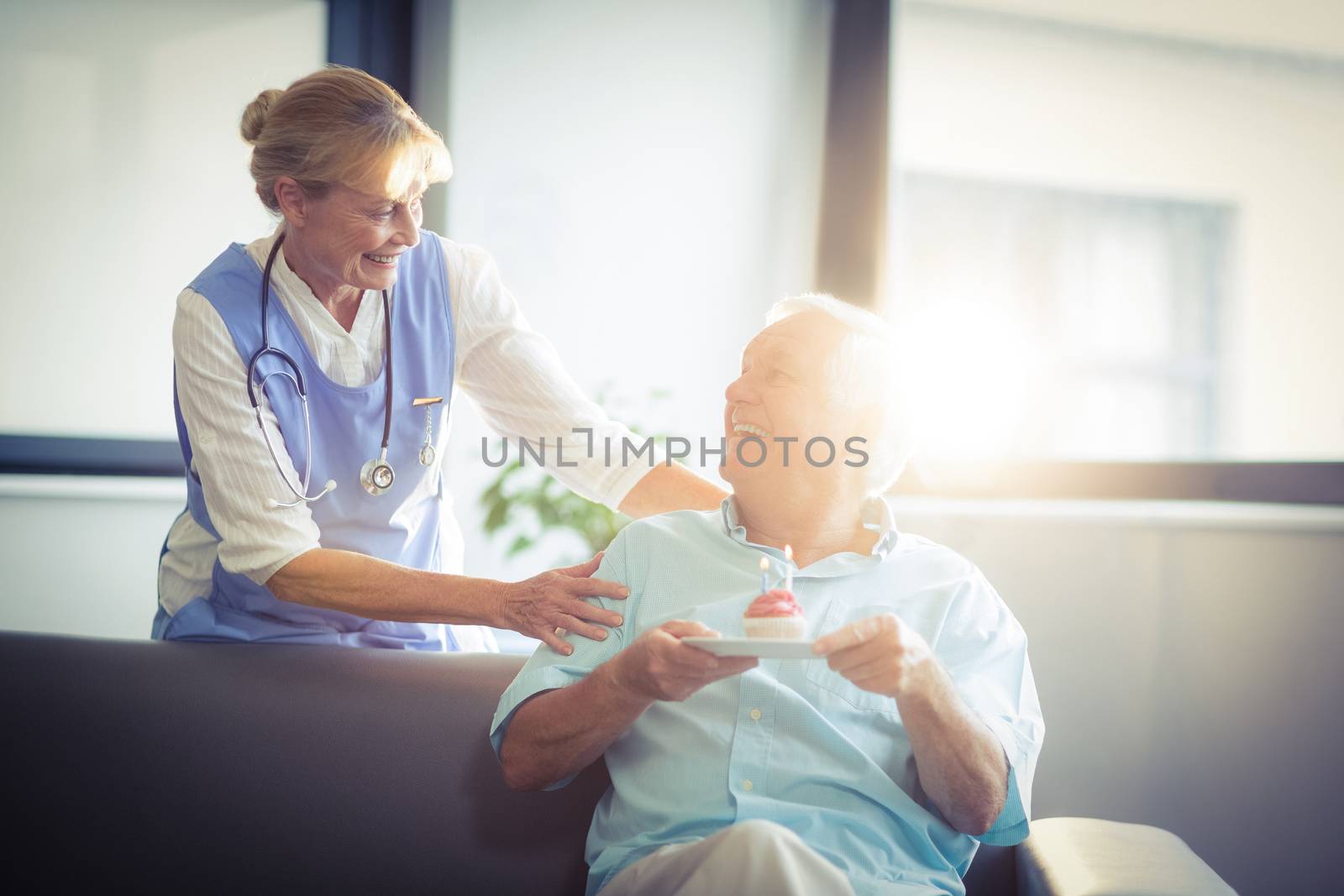 Senior man holding an cupcake while celebrating his birthday in hospital with a female doctor