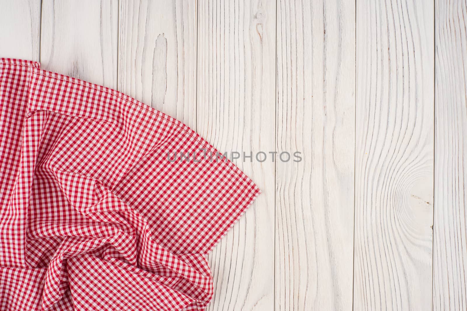 Red folded tablecloth over bleached wooden table. Top view.