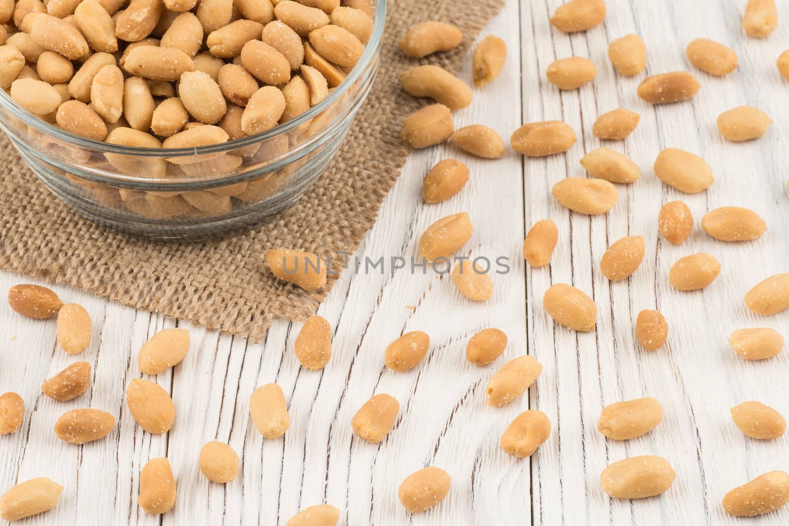 Salted peanuts in a glass bowl on the old wooden table. Selective focus.