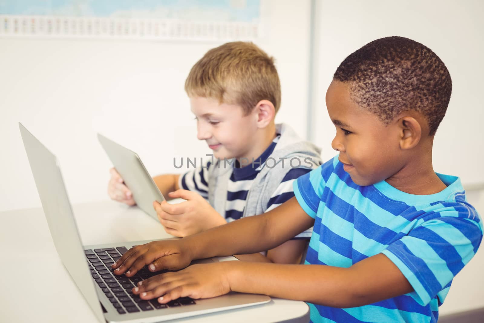 School kids using a laptop and digital tablet in classroom by Wavebreakmedia