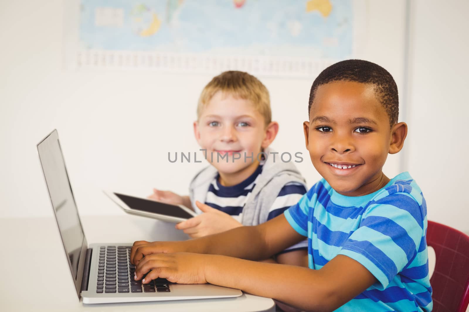 Portrait of smiling kids using a laptop and digital tablet in classroom at school