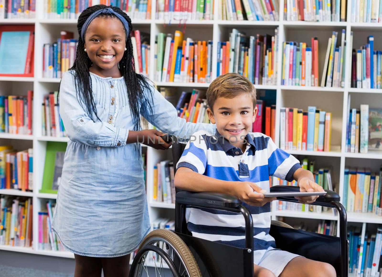 Happy schoolgirl standing with schoolboy on wheelchair by Wavebreakmedia