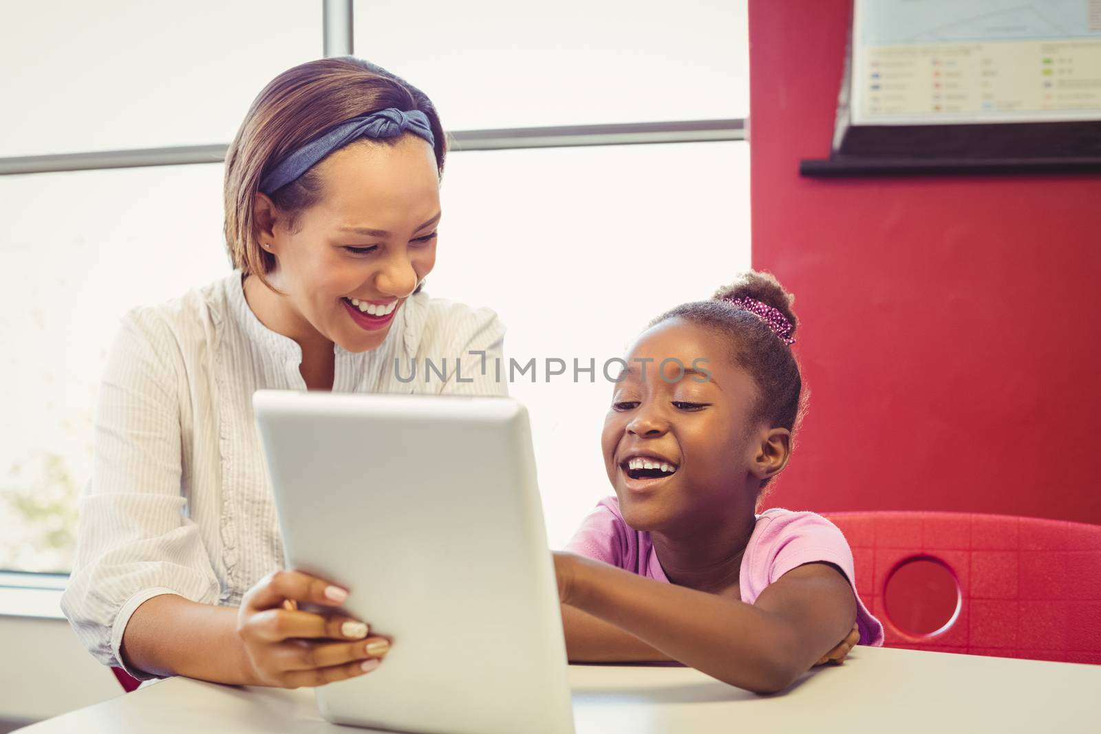 Teacher and school girl using digital tablet in classroom at school