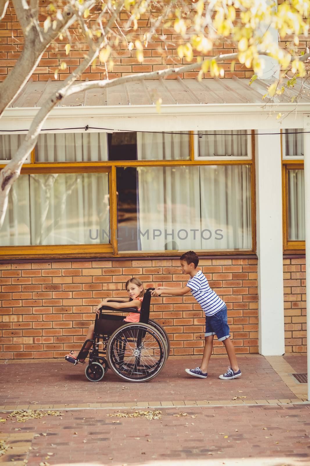 Schoolboy pushing a girl on wheelchair in school corridor