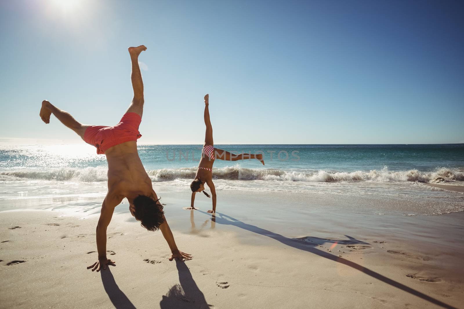 Couple performing somersault on beach in summer