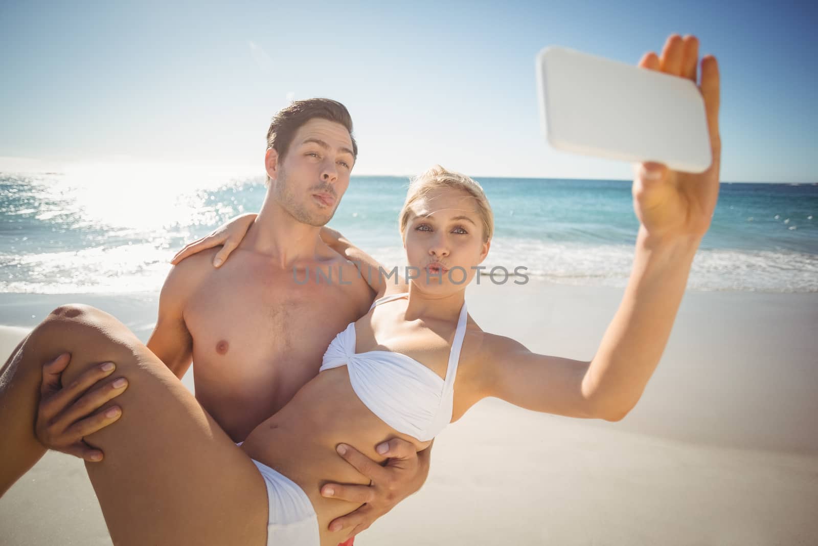 Happy young couple taking selfie with mobile phone on beach