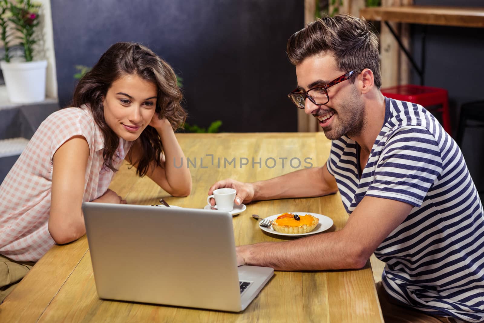 Young couple sitting at table using laptop in cafeteria