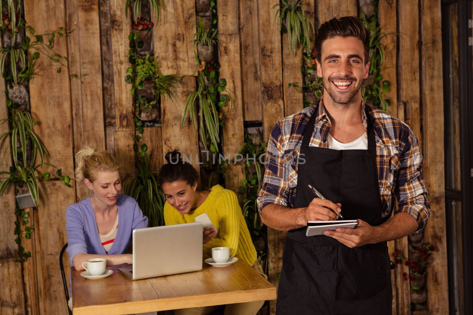 A waiter is taking the order in front of the two friends in a coffee shop