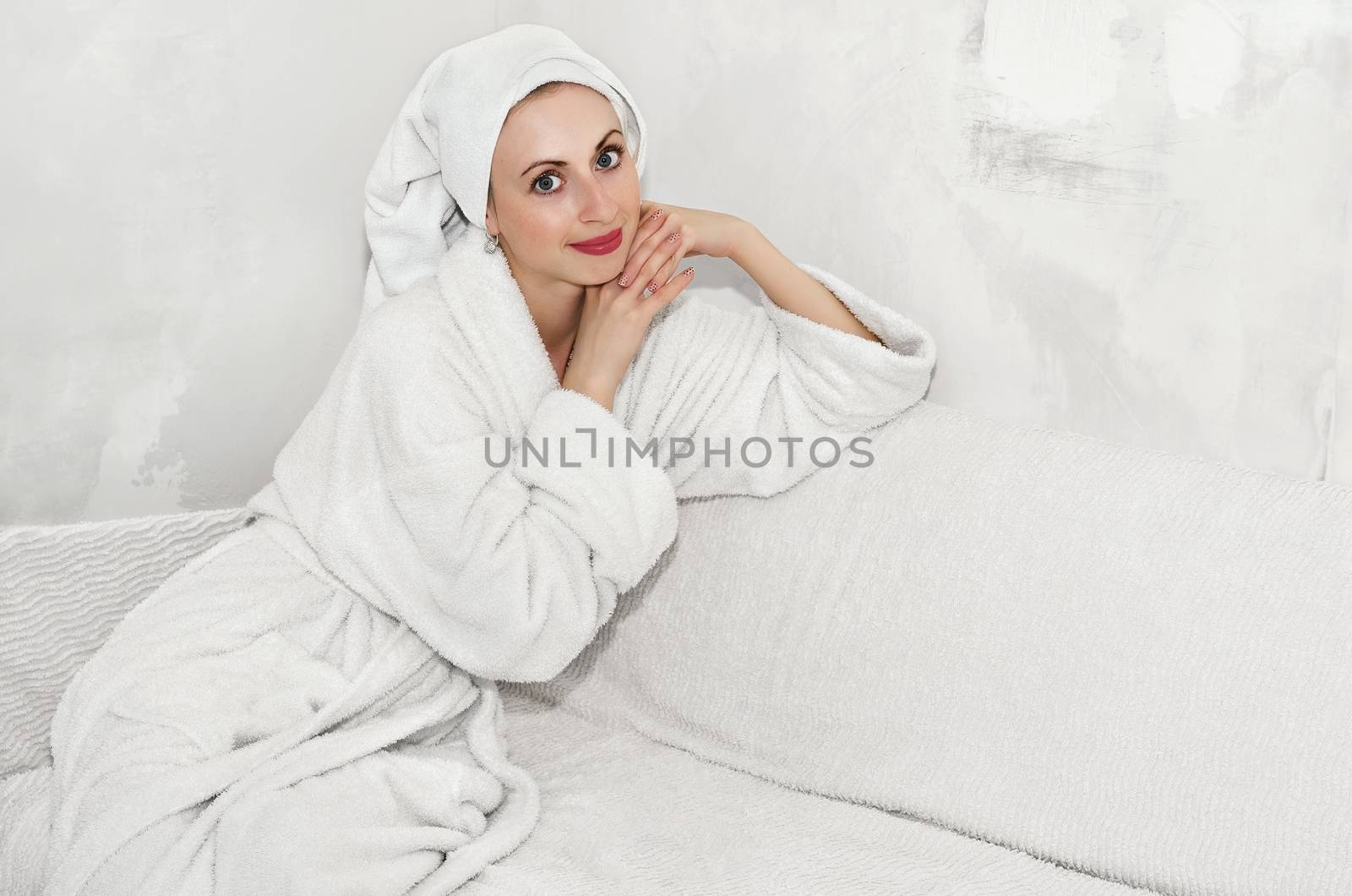 Beautiful girl sitting on the sofa in a fluffy Bathrobe in a room with no Wallpaper on the walls needed to be repaired. White background, high key. Plenty of space for text.