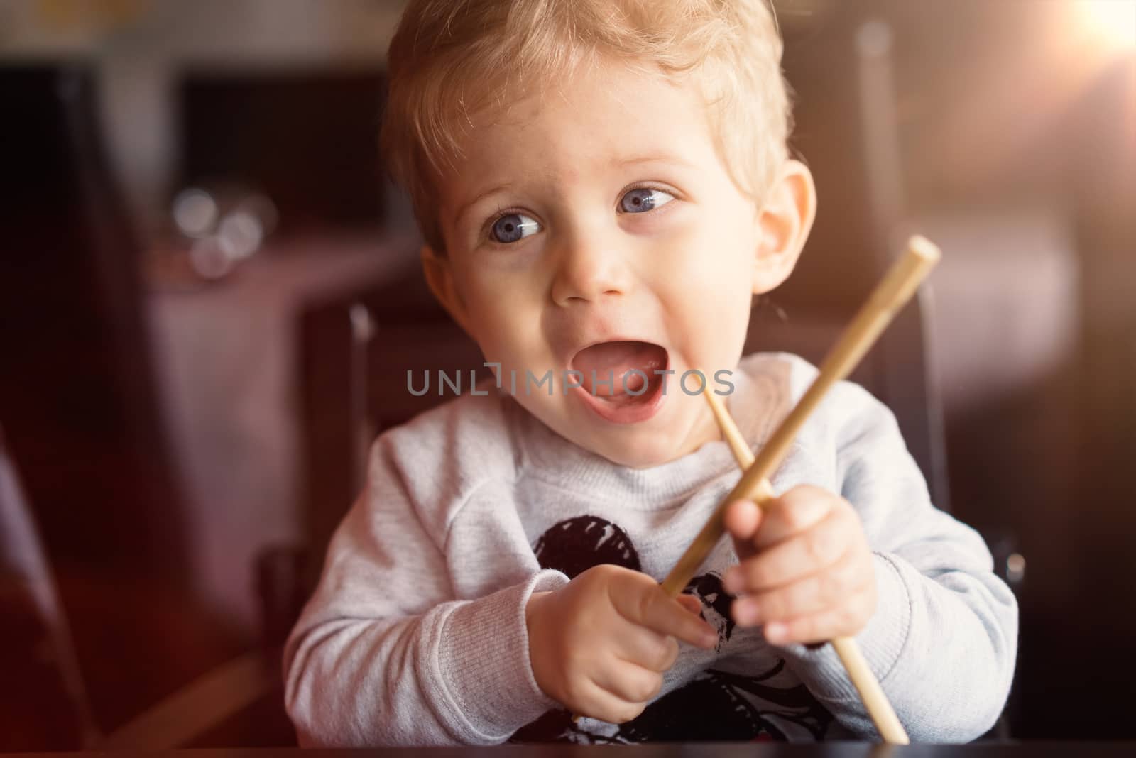 Baby boy sitting in high chair and plays with chopsticks at chinese restaurant.Used split toning and flare for vintage style.