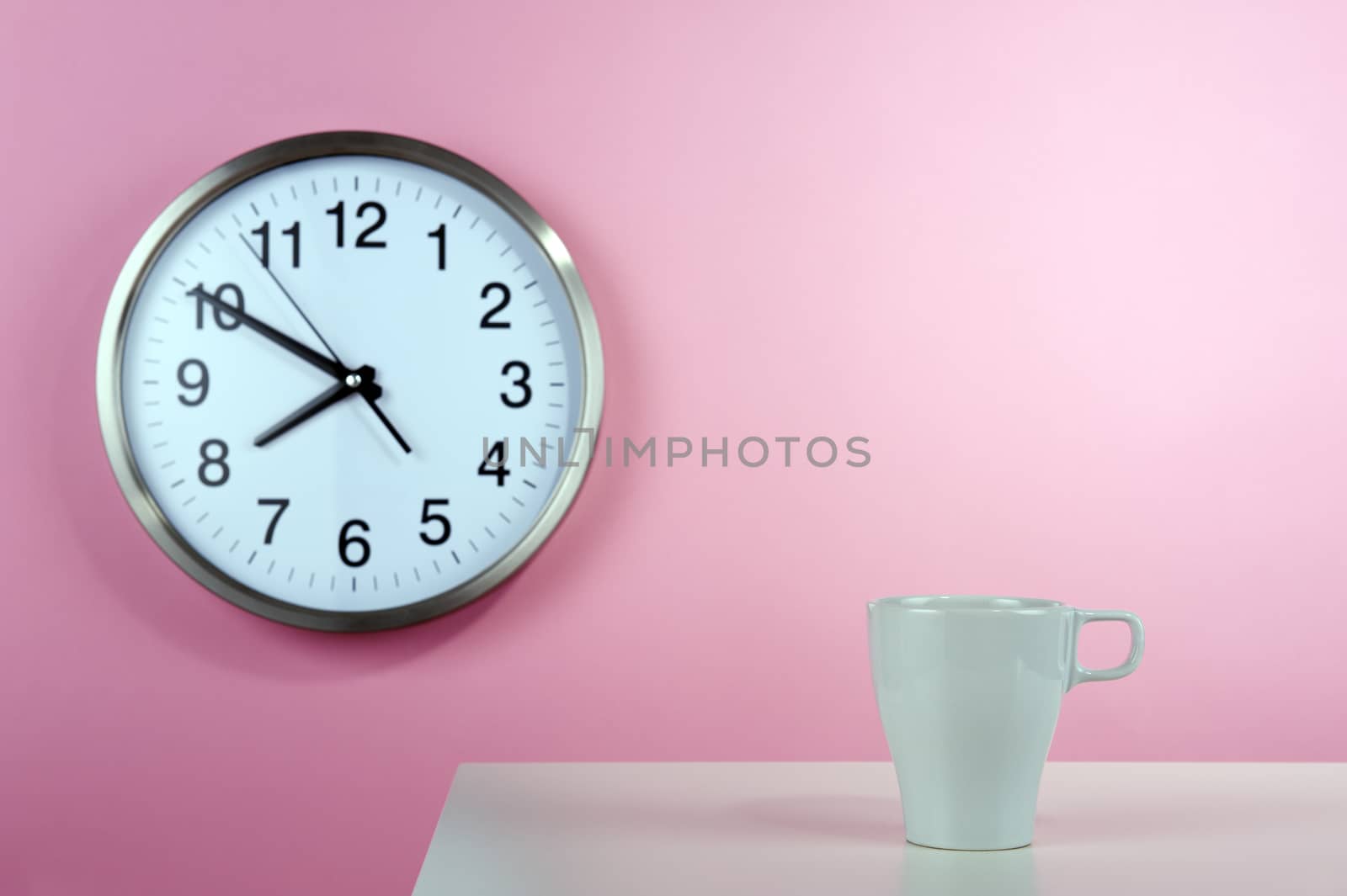 Empty white cup on the background of a pink wall with a clock