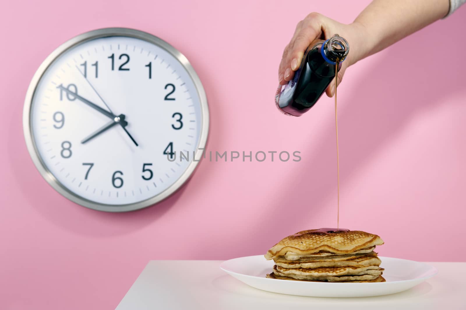 American pancakes with maple syrup on a pink background with a clock