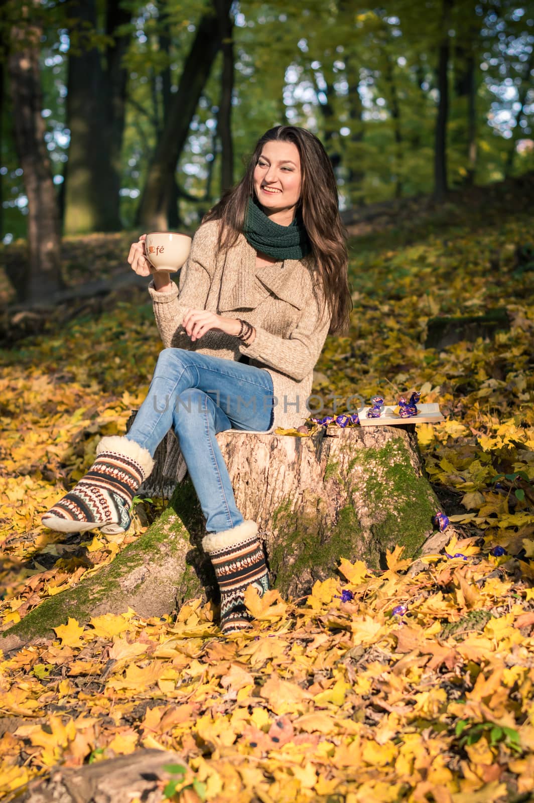 girl with a cup of coffee sitting on a tree stump in autumn Park