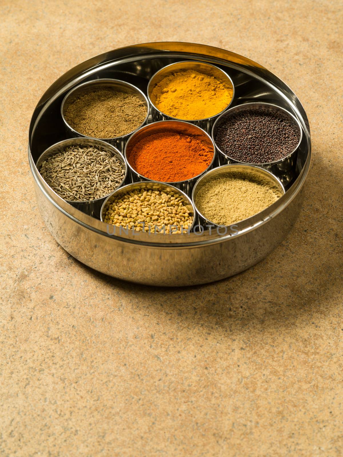 Photo of a Masala box containing turmeric, fenugreek, coriander, garam masala, black mustard seeds, red chilli, and cumin seeds.