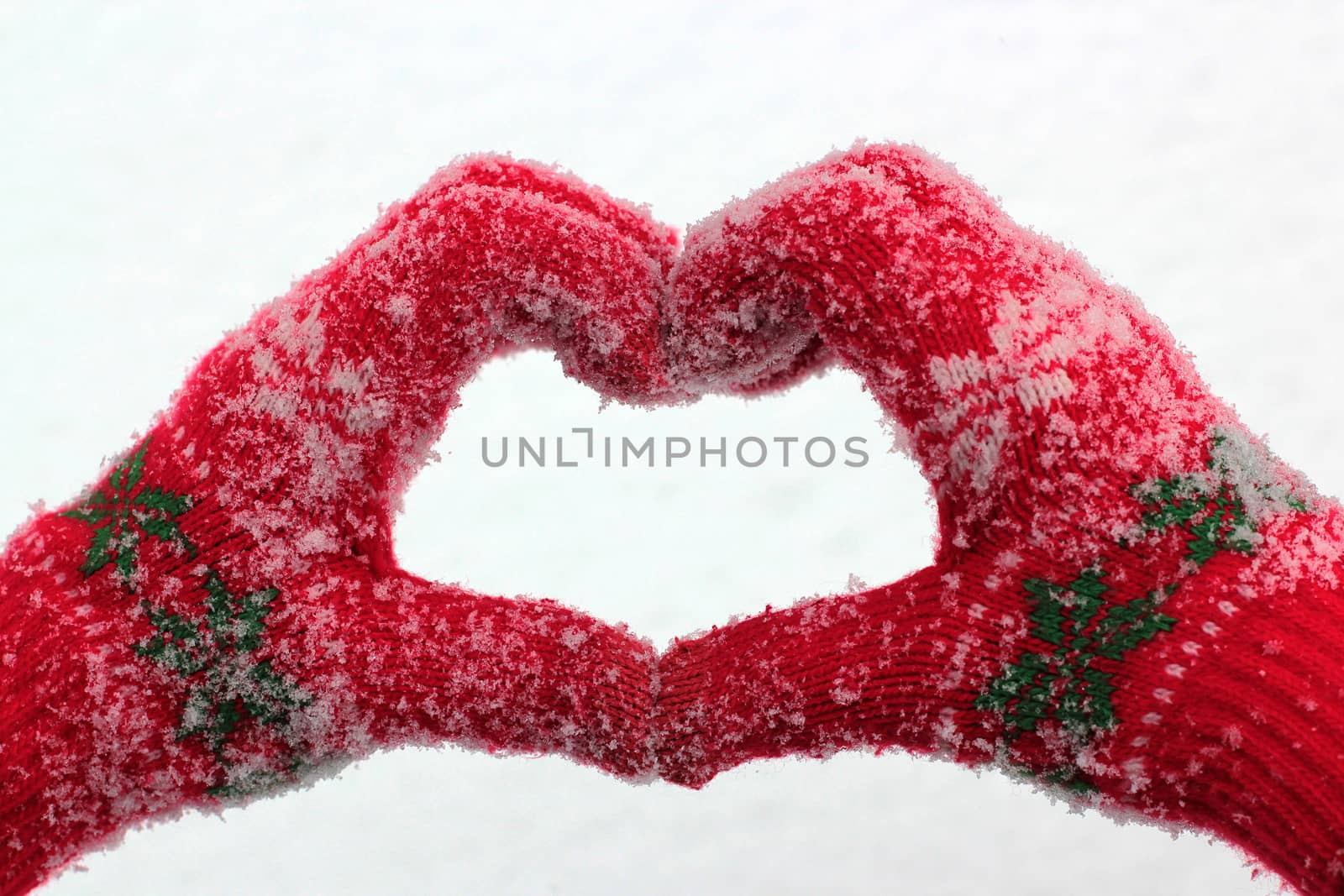 hands in snow-covered gloves in the form of heart against the background of snow