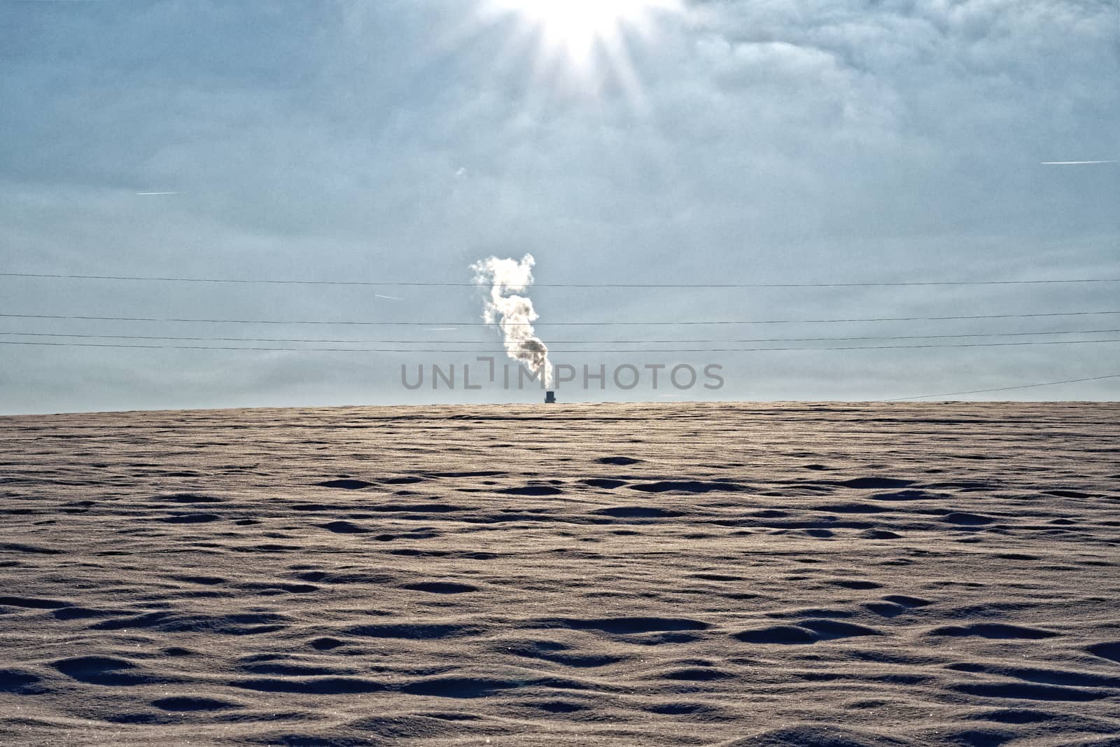 The smoking chimney in the distance in a snowy landscape
