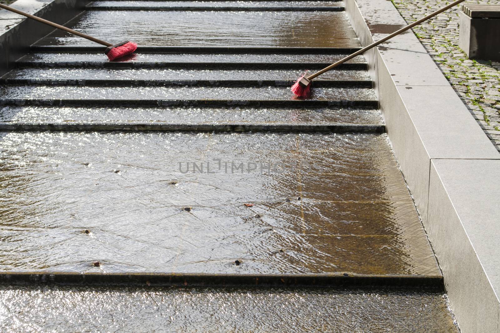 Two road brooms stand in a water channel.