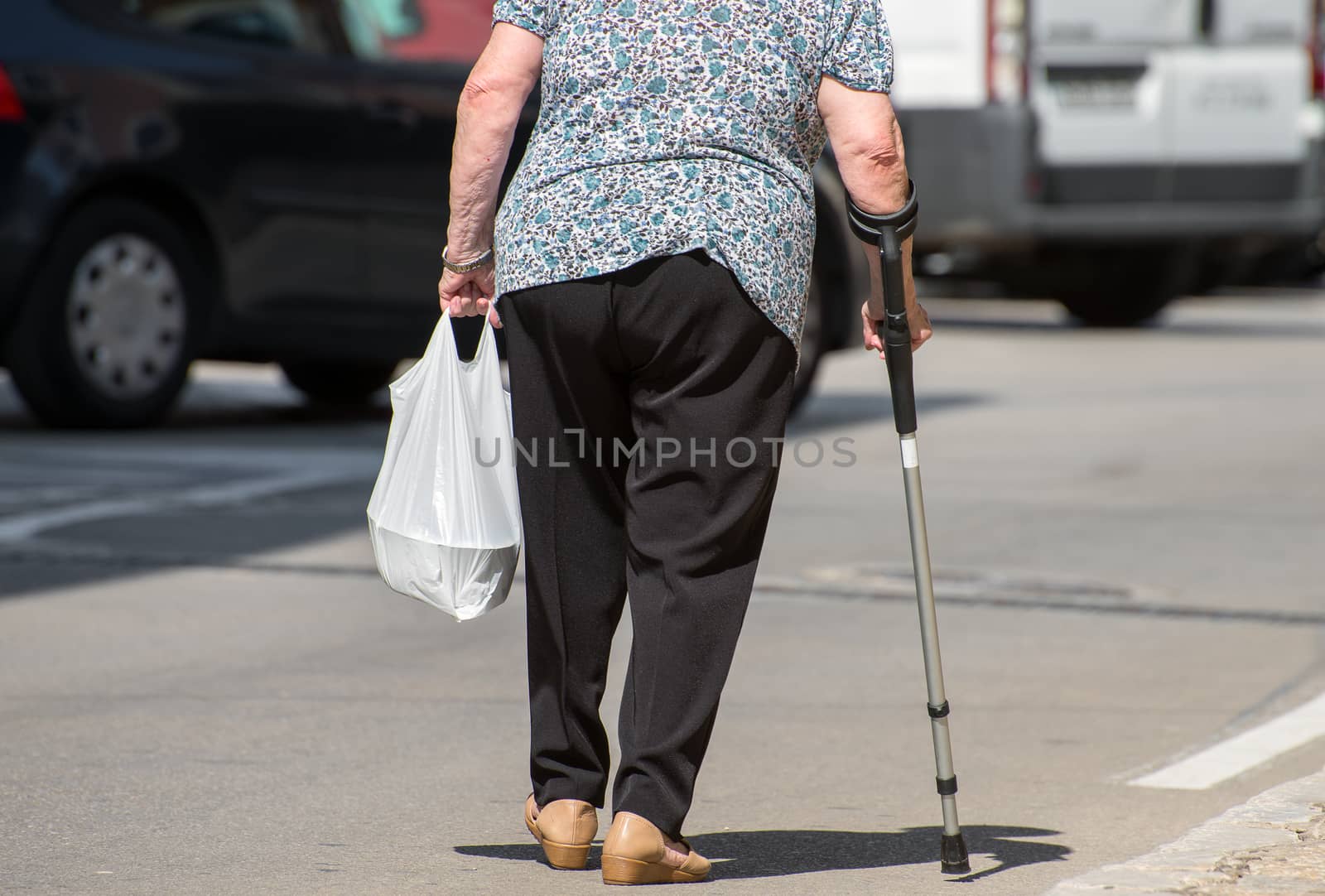 Elderly woman with crutch on the street.