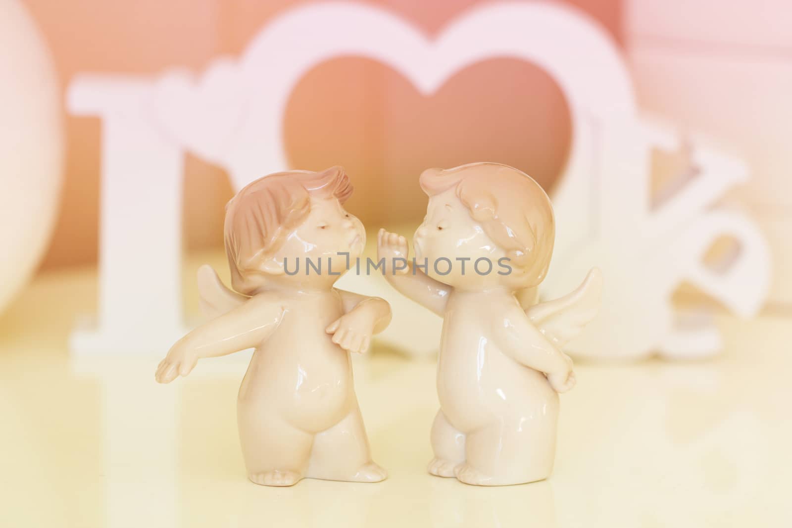 Two angels  with white wooden letters forming word LOVE on background 