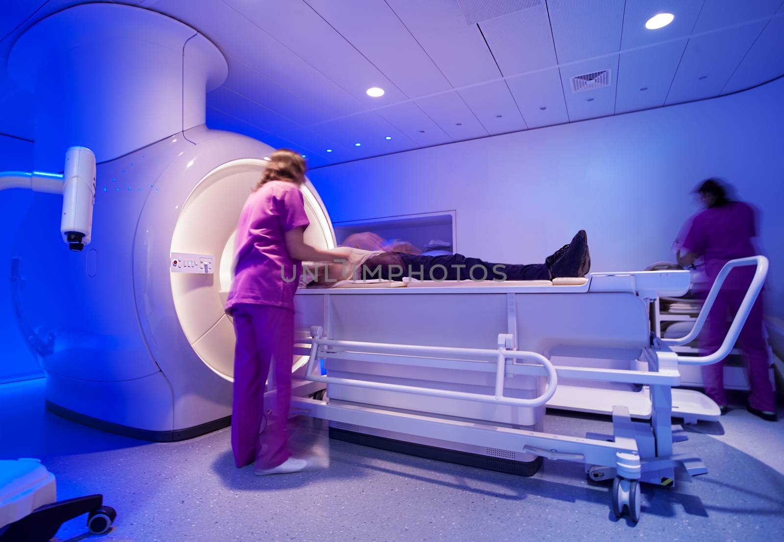 A super powerful modern magnetic resonance scanner is being prepared by nurses for scan with a patient.