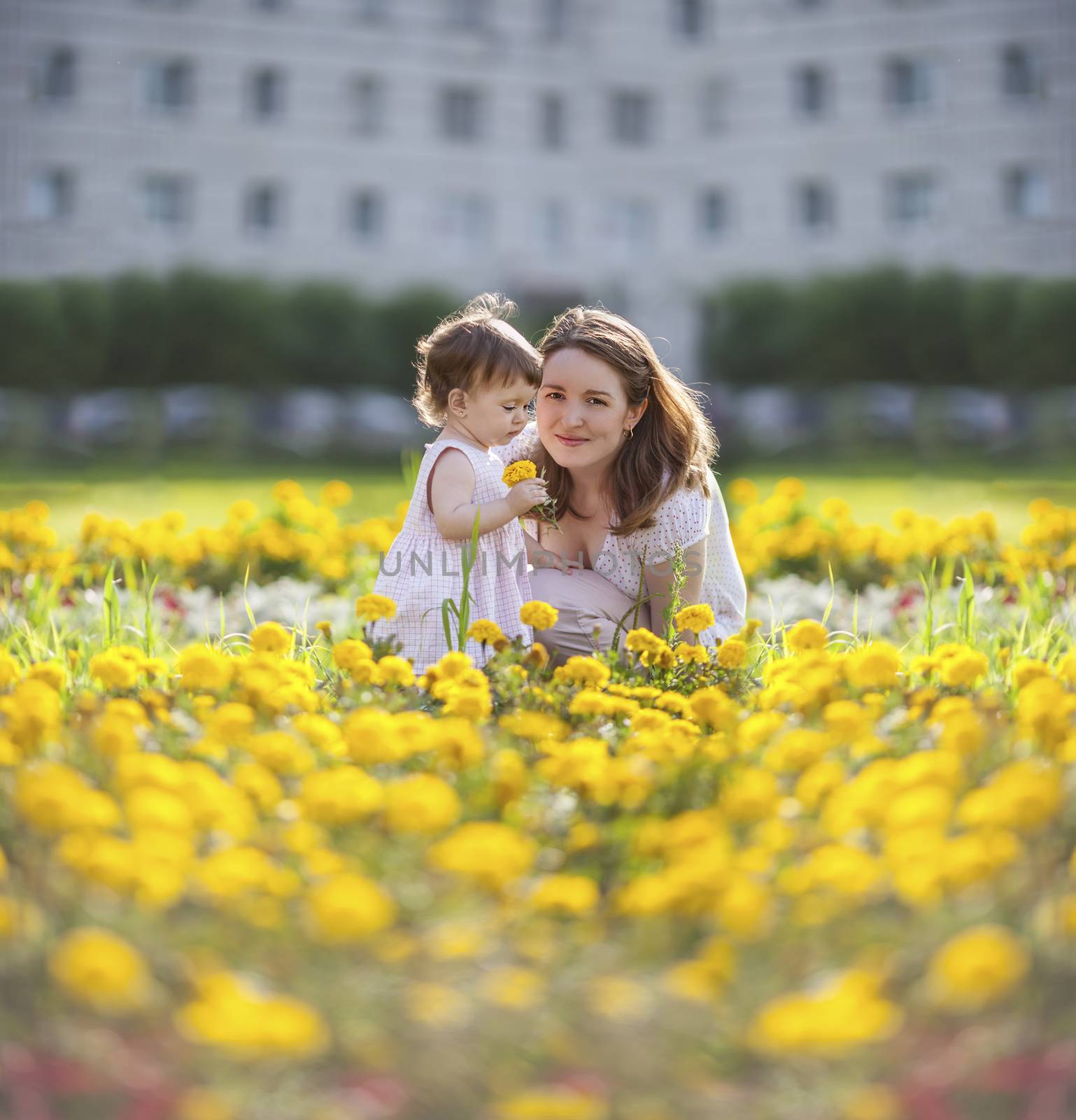 Happy mother sitting with daughter in yellow flowers meadow